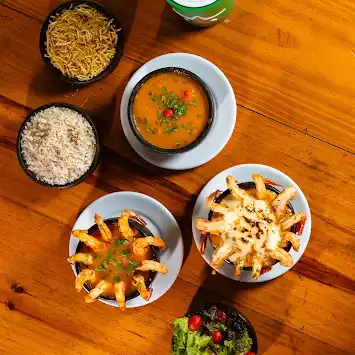 Pratos de camarão, moqueca, arroz e salada na mesa de madeira