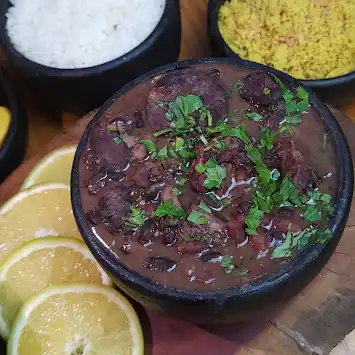 Feijoada servida na panela de barro com arroz, farofa e laranja